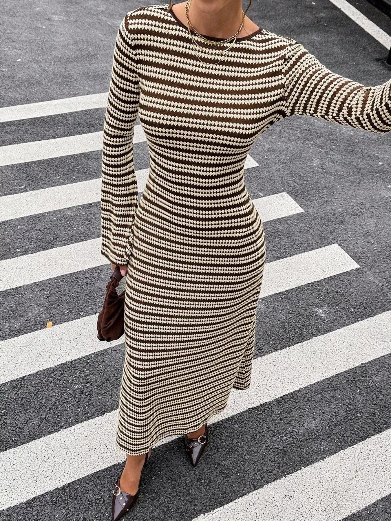 On-model front view of the brown and cream striped sweater dress with one arm extended