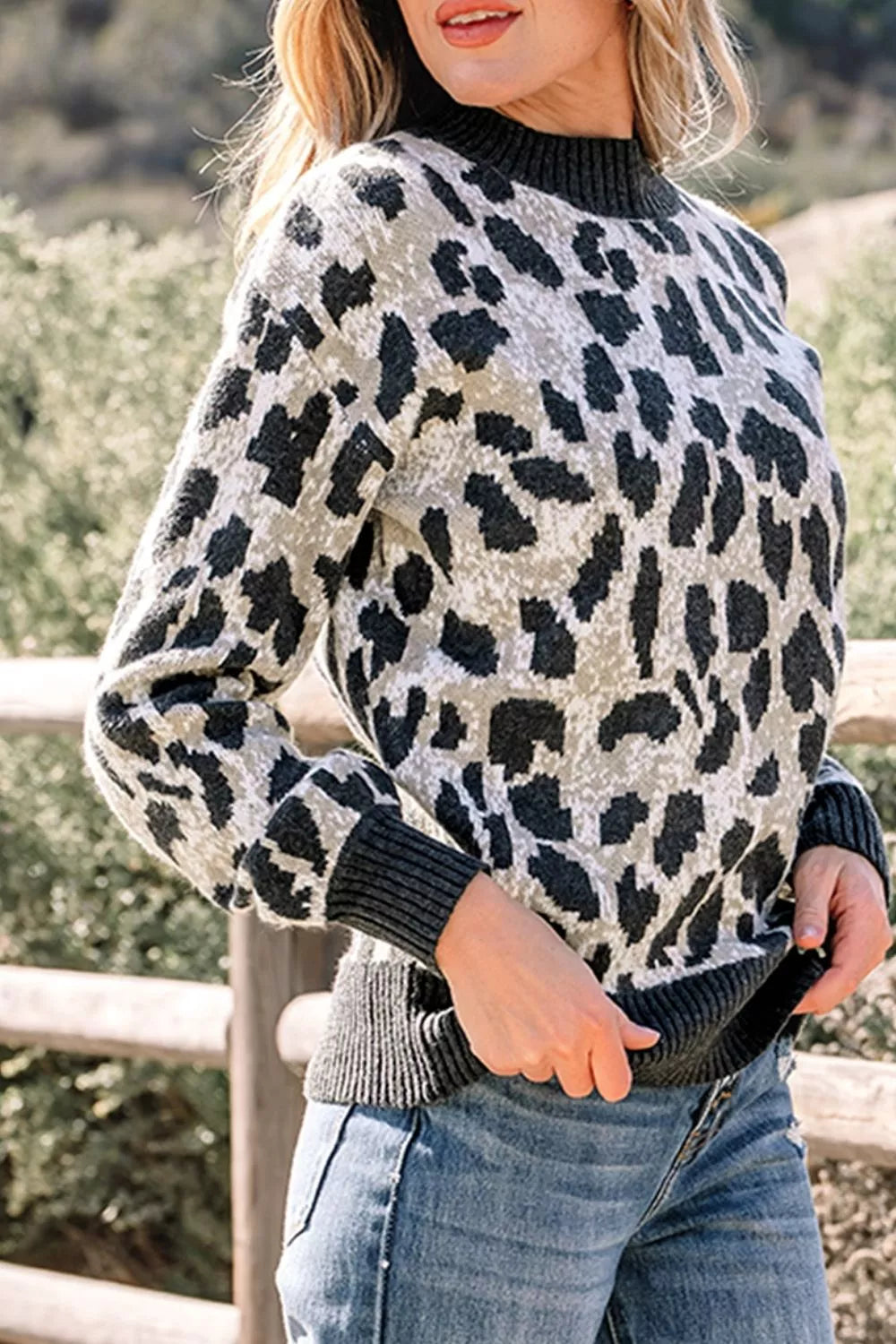 Front angled view of the gray and black leopard print baggy sweater with ribbed collar, outdoors.