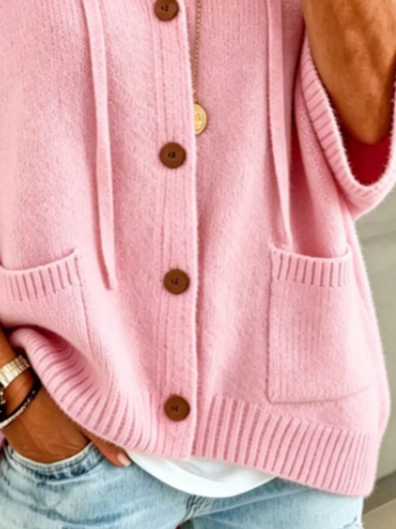 Detail view of the pink cardigan showing brown buttons, patch pockets and ribbed hem
