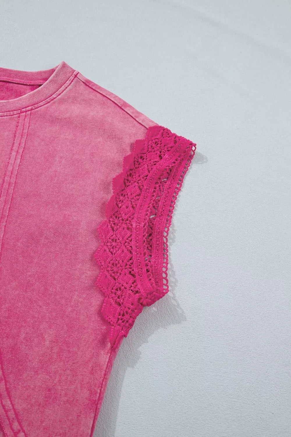 Close-up detail of pink mineral-wash top featuring raw seam accents and intricate lace-trim cap sleeve