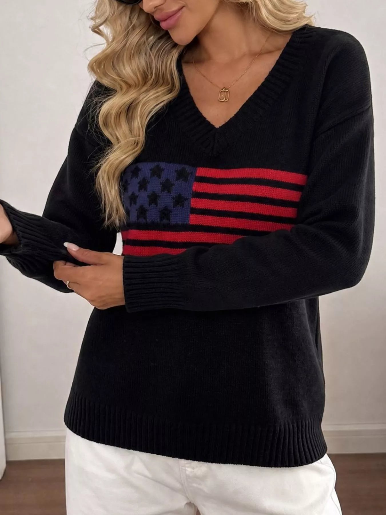 Side front view of black V neck knit sweater with American flag print and ribbed cuff.