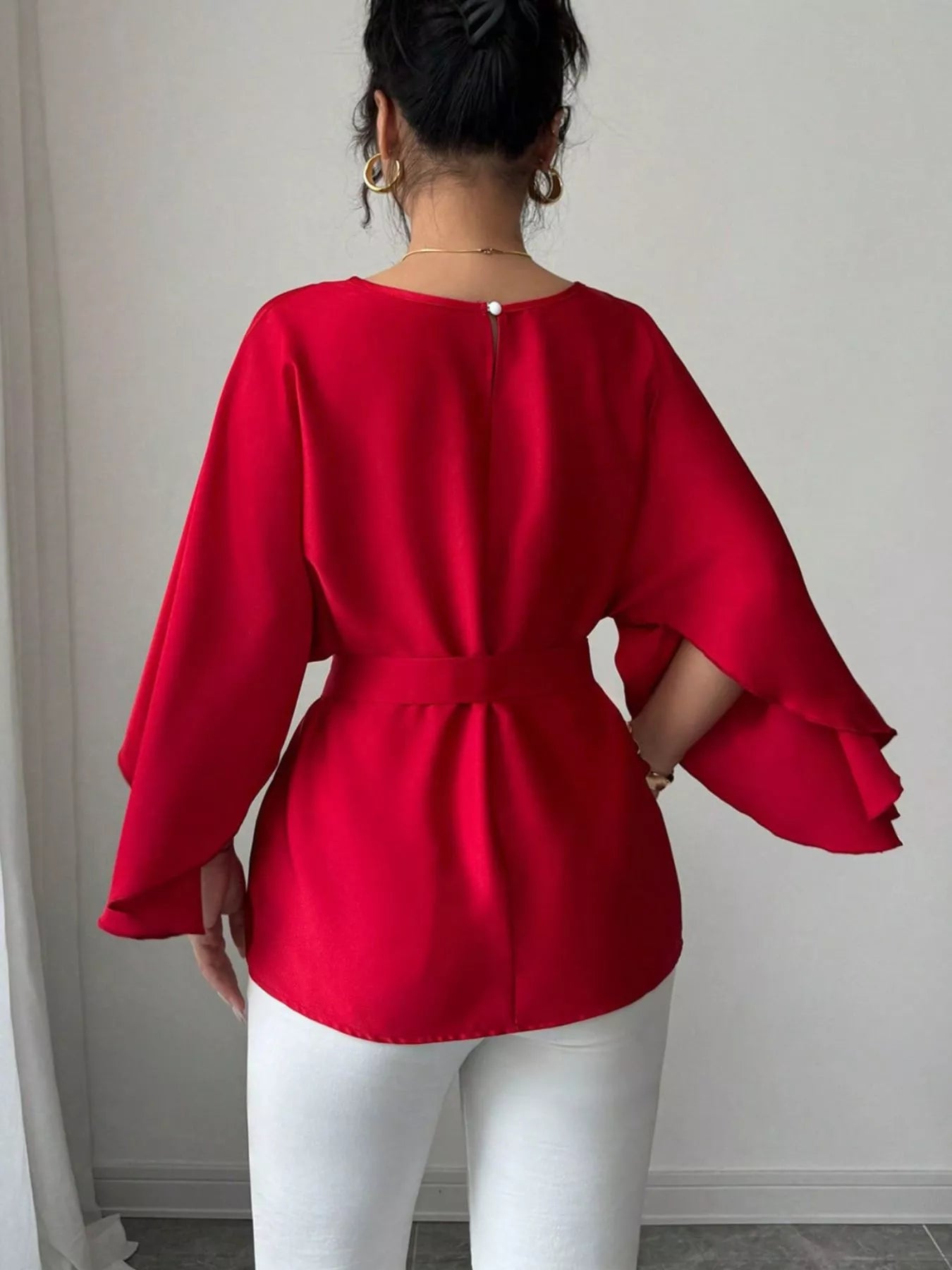 Back view of red batwing sleeve blouse showing button keyhole neckline and belted waist