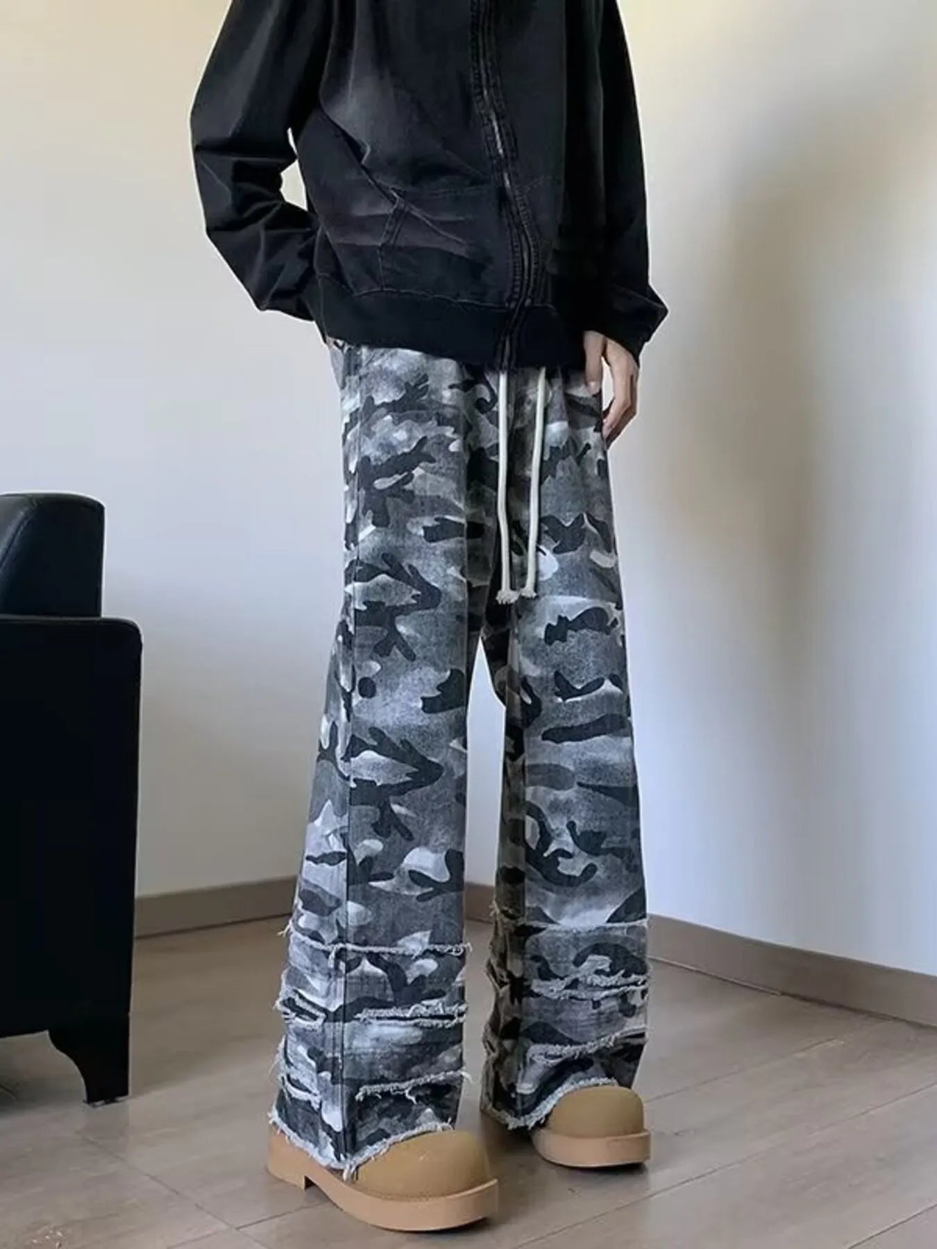 Three-quarter view of men's grey camouflage wide leg jeans with frayed raw hems, styled on model.