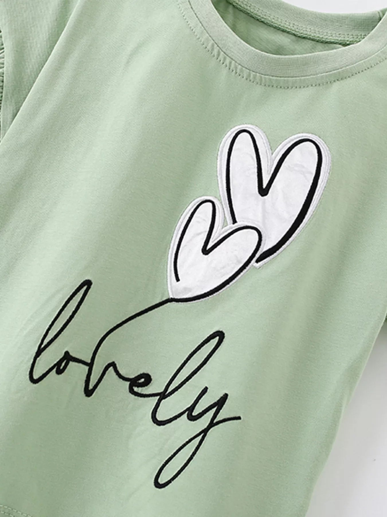 Close view of the white heart appliques and black lovely lettering on the sage children's T-shirt