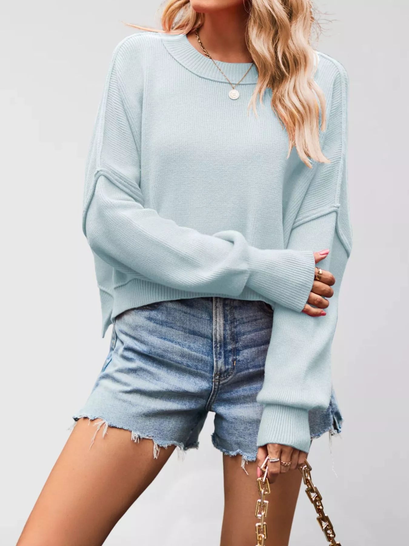Front view of a light blue crew neck dropped shoulder sweater with ribbed cuffs worn with denim shorts.