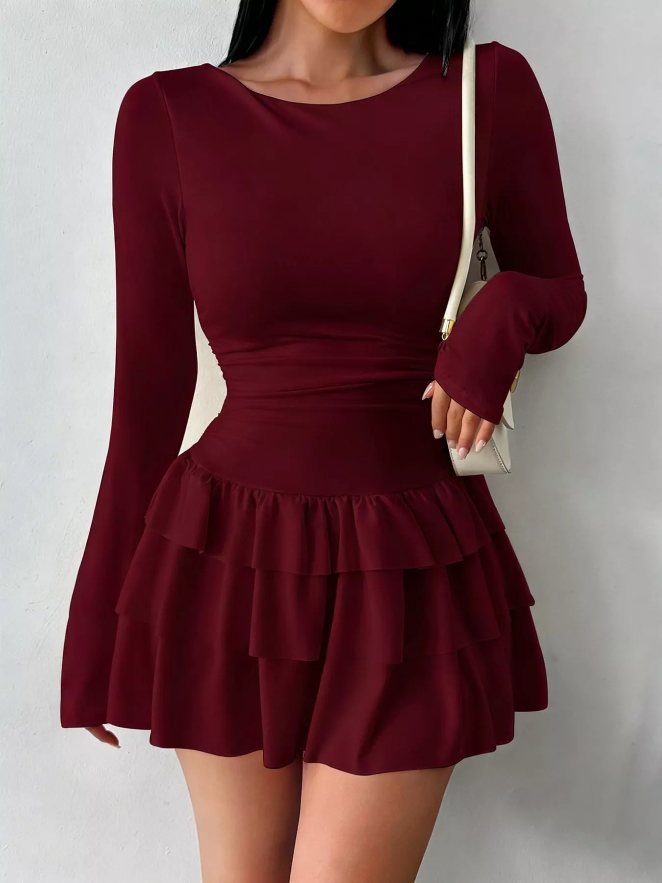 Burgundy layered ruffle long sleeve mini dress worn front facing with a white shoulder bag
