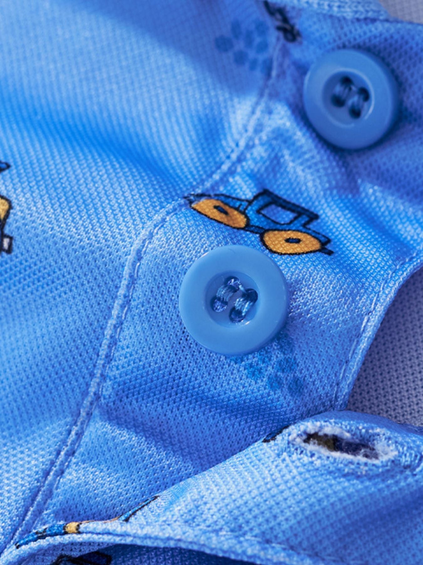 Close view of the polo buttons and small tractor print on the blue children's polo shirt