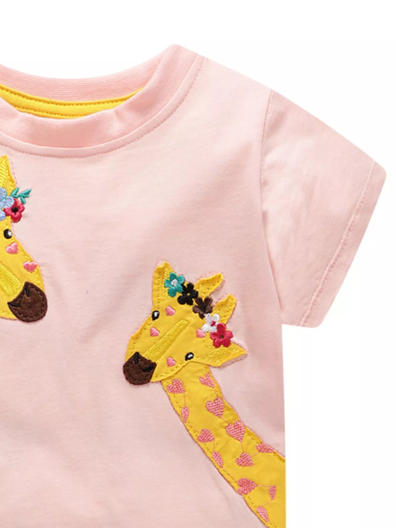 Angled close view of a yellow giraffe applique with flowers on blush pink fabric