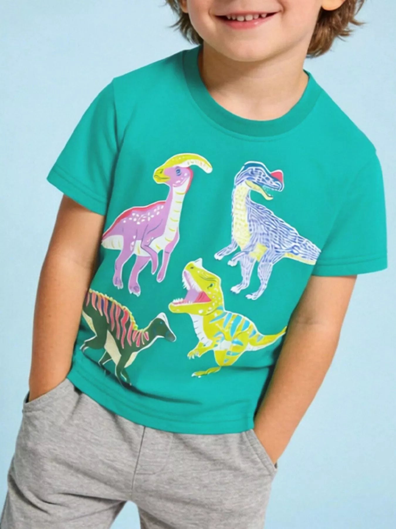 On-model front view of turquoise children's crew neck t-shirt with four colorful dinosaur prints