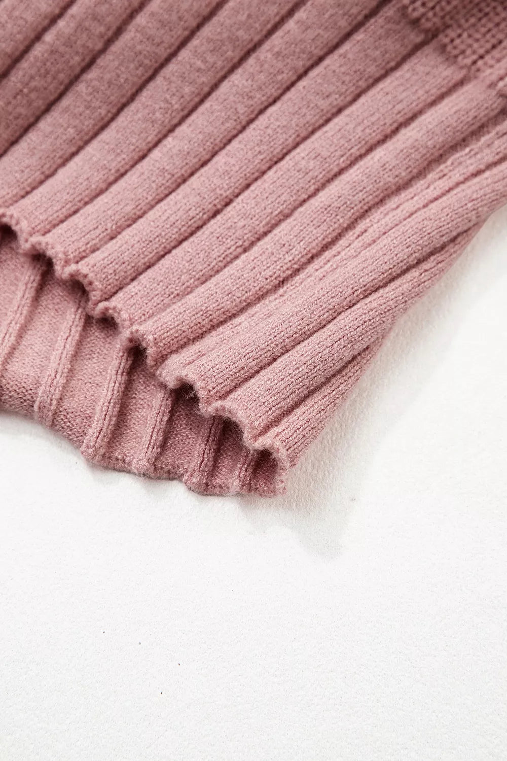 Close-up of the scalloped ribbed hem on a dusty pink knit cardigan