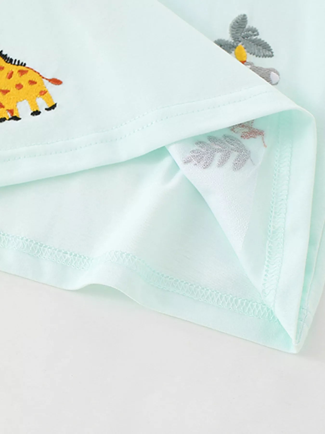 Close-up of the mint blue polo hem stitching beside an embroidered giraffe motif