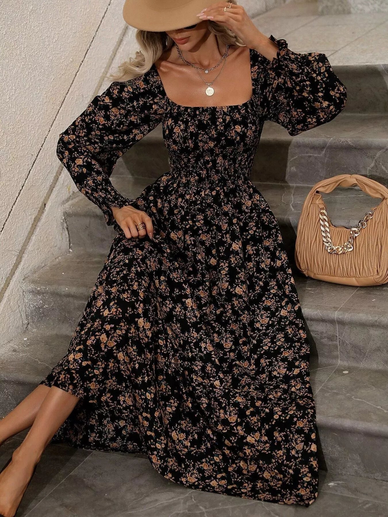 Black floral midi dress with smocked bodice, model seated on stone steps
