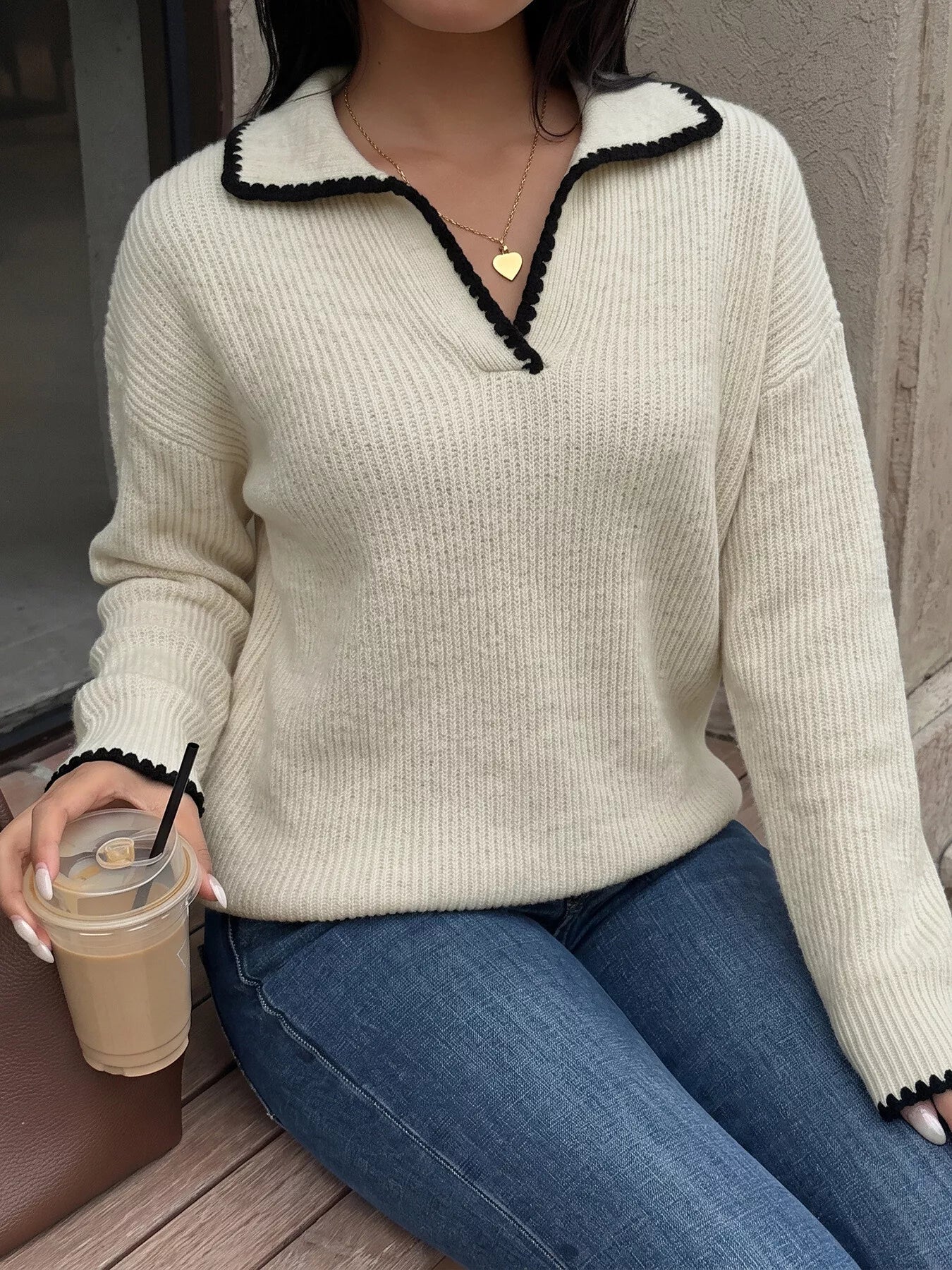 Seated front view of a cream dropped shoulder sweater with black scalloped collar trim