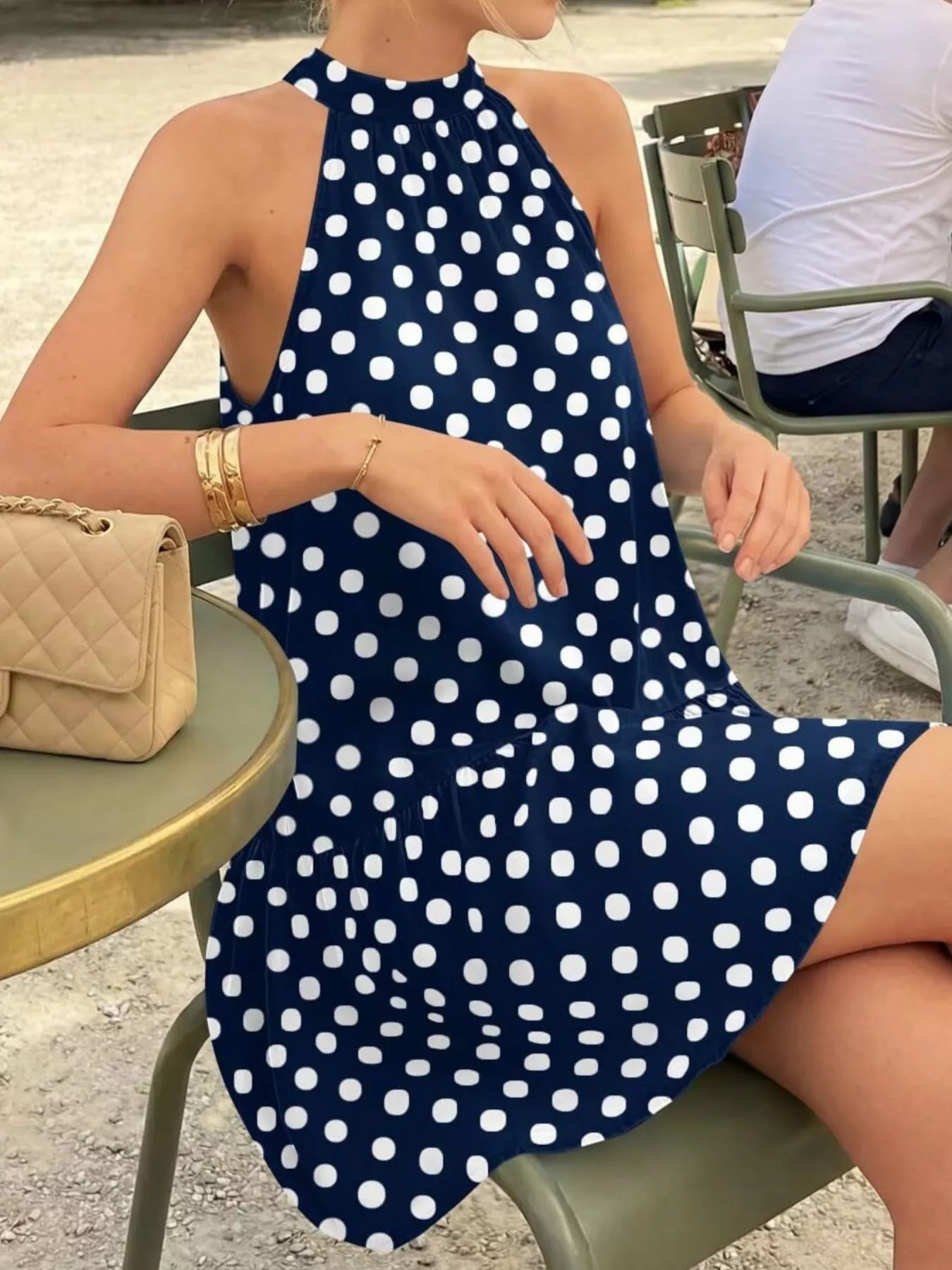 Navy blue polka dot halter neck mini dress worn seated in side view outdoors