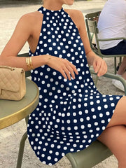 Navy blue polka dot halter neck mini dress worn seated in side view outdoors