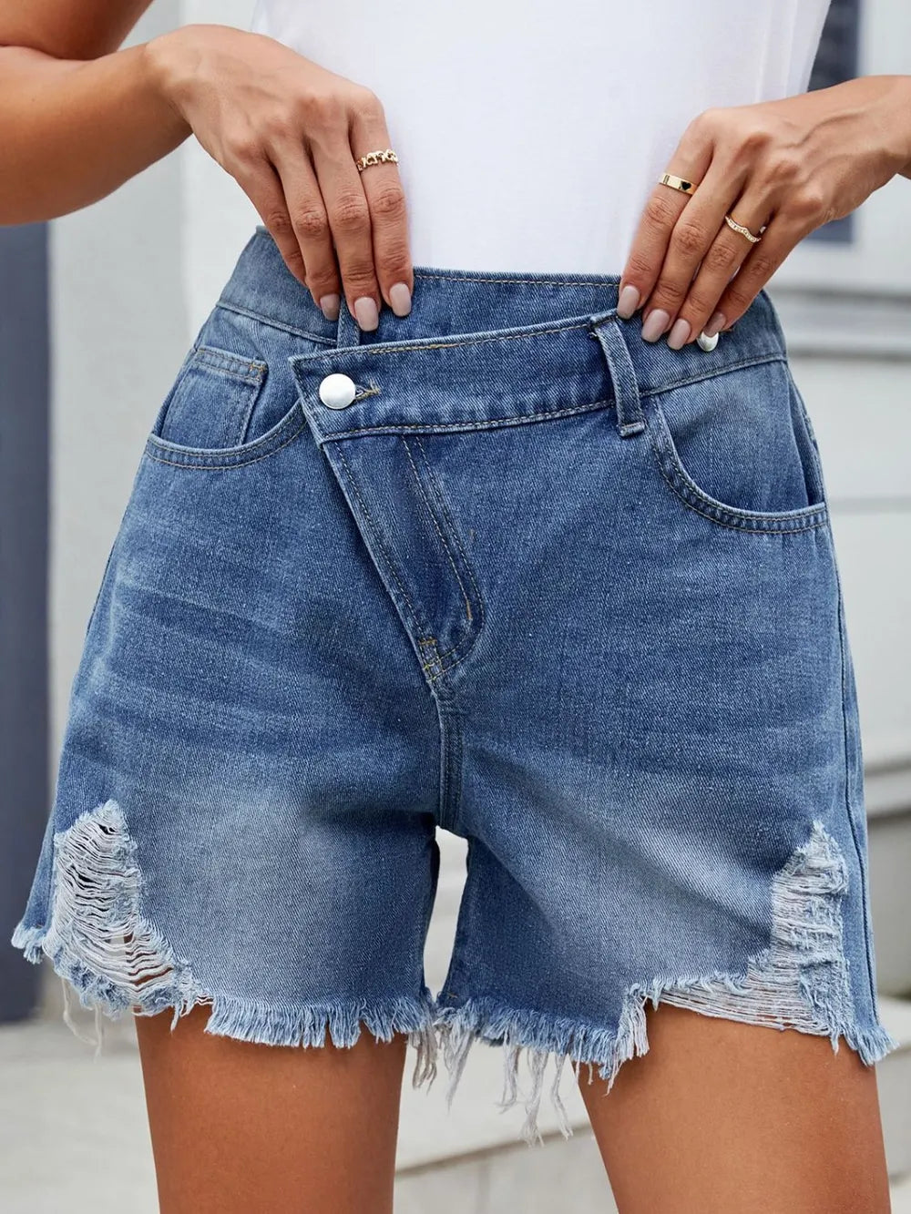 Women's distressed denim shorts with an asymmetrical waist, washed detailing, and raw hems.