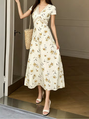 Model wearing a yellow floral midi dress with lace waist detail and woven straw bag