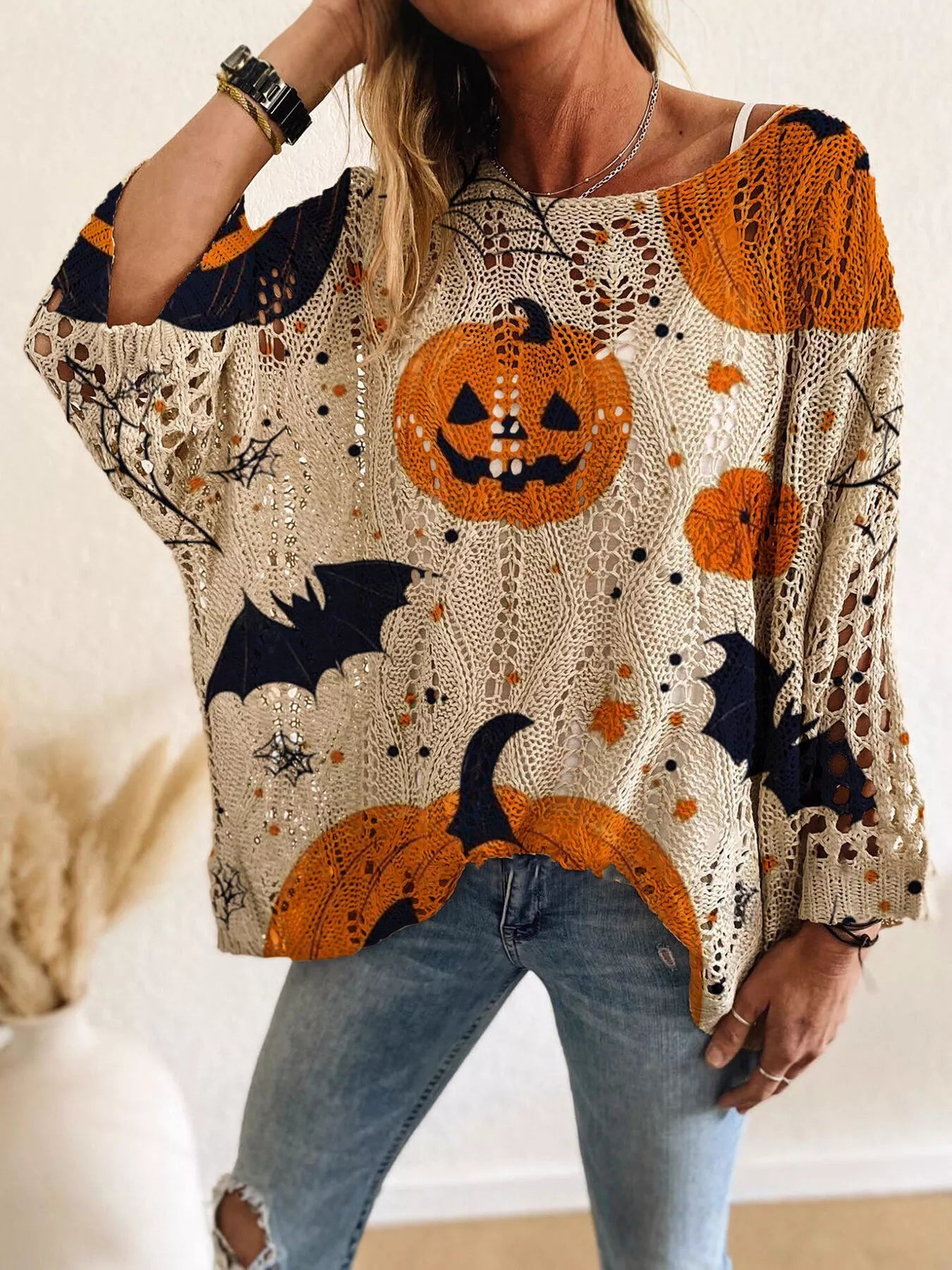 Front view of a beige openwork knit cover up with orange jack o lanterns, bats, and spider webs.