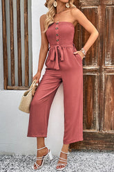 Women's watermelon pink strapless jumpsuit with smocked detailing, decorative buttons, a belt, and pockets.