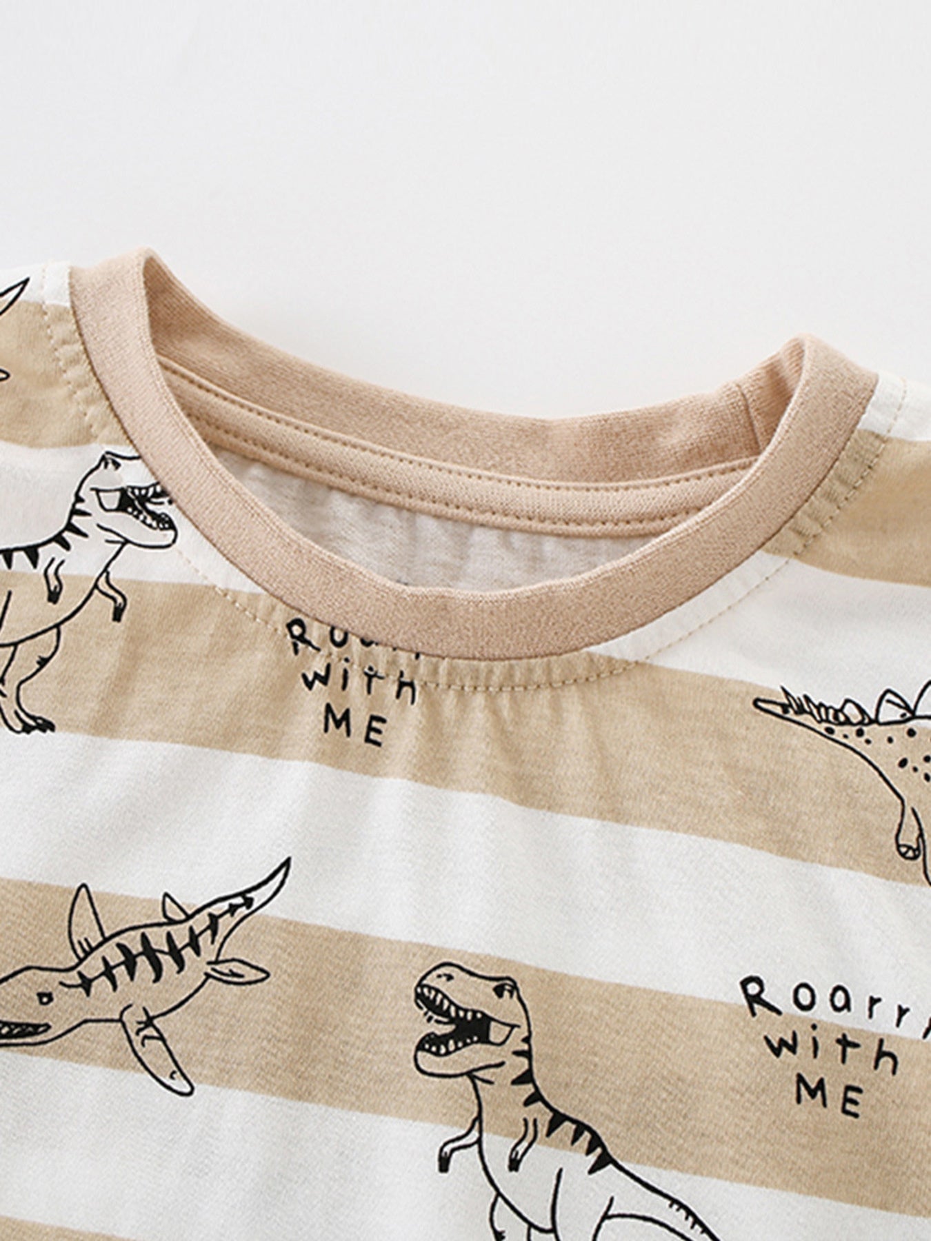 Close-up of the tan ribbed crew neckline on a striped children's dinosaur print T-shirt