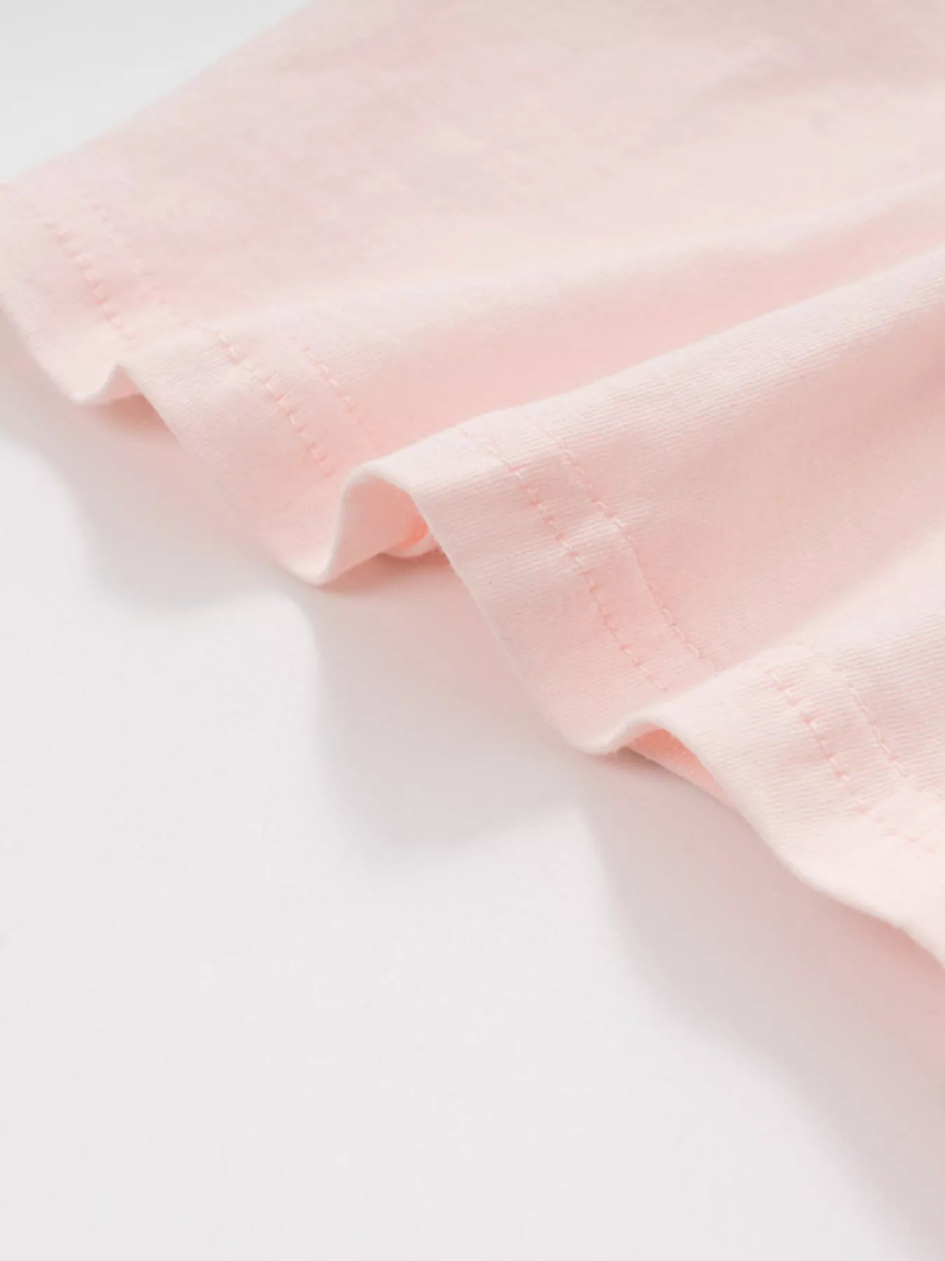 Close-up of the blush pink fabric and stitching at the hem of the children's t-shirt