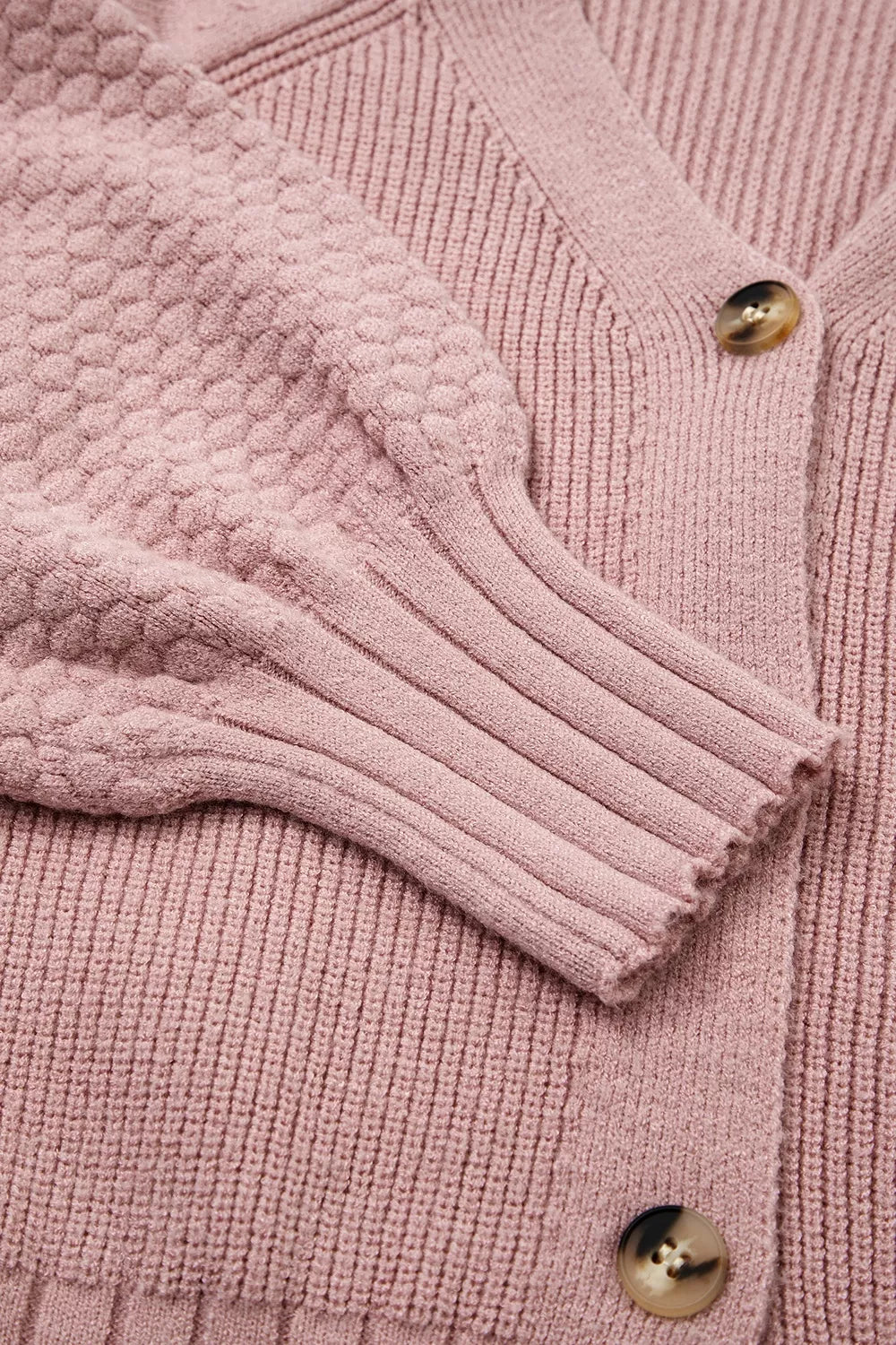 Flat lay close-up of the textured sleeve and ribbed cuff on a dusty pink cardigan