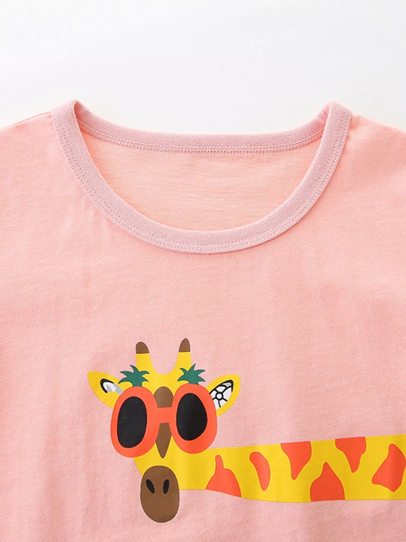Close-up of pale blush round neckline above a cartoon giraffe wearing orange sunglasses