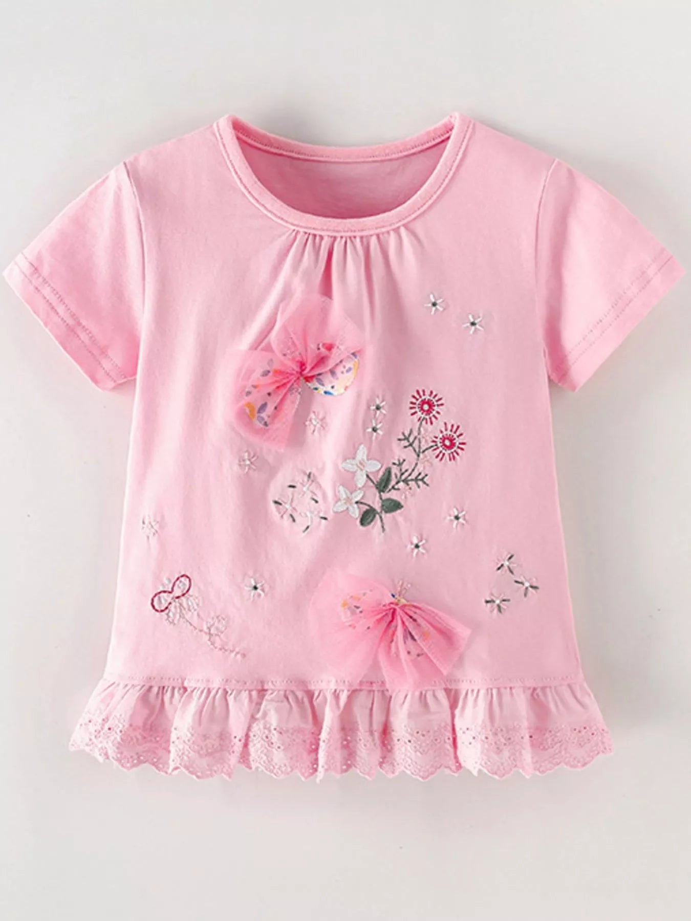 Flat lay front view of a children's blush pink t-shirt with tulle bows and embroidered flowers above a ruffled hem