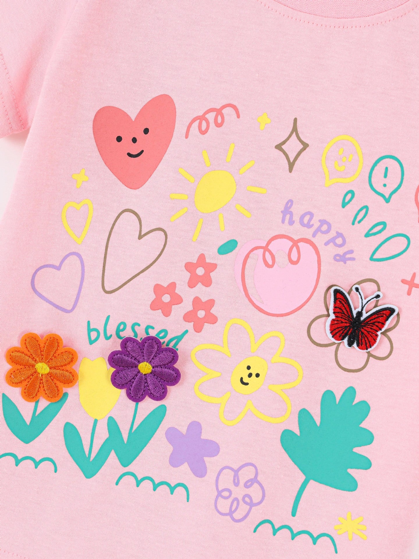Close-up of colorful cartoon print on pink children's t-shirt, with hearts, sun, flowers and butterfly