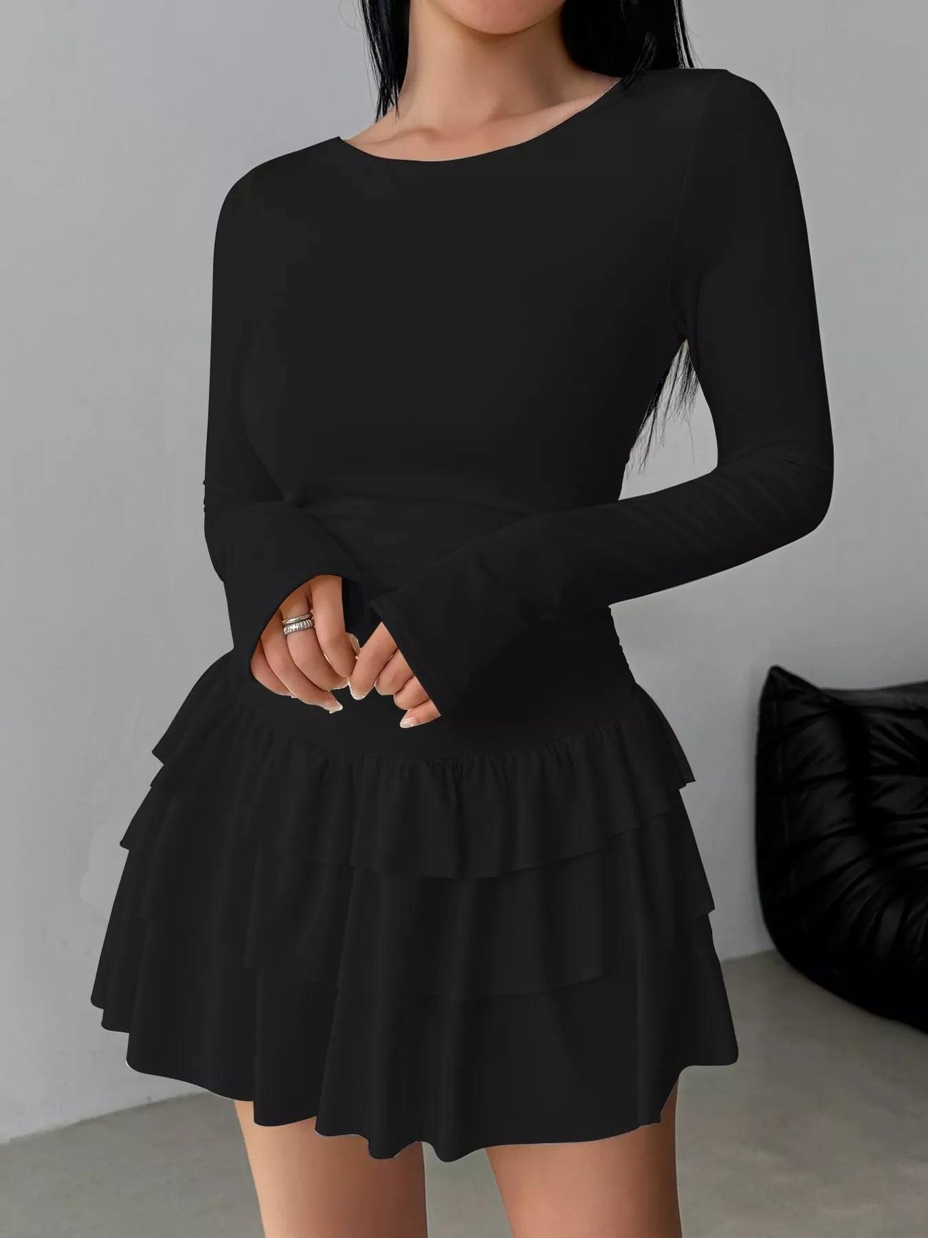 Black layered ruffle long sleeve mini dress worn front facing with hands clasped at the waist