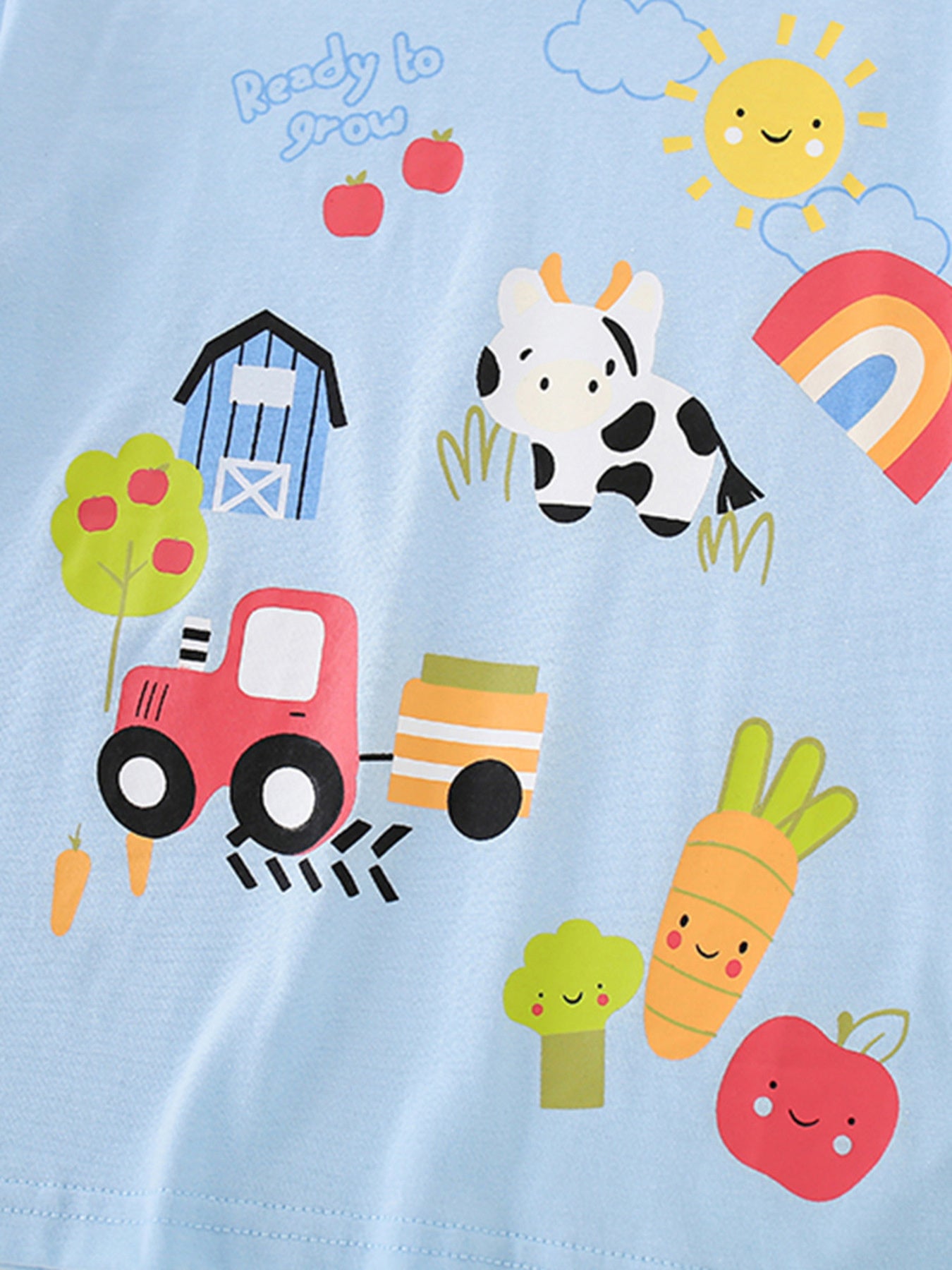 Close-up print detail showing the cow, tractor, carrot and apple on light blue children's T-shirt