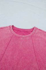 Close-up front detail of a pink mineral-wash top featuring raw seam detailing and a ribbed crew neckline