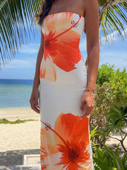 Front view of an orange floral print strapless bodycon maxi dress on a beach