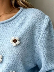 Close-up detail of sky blue textured knit with a white floral applique