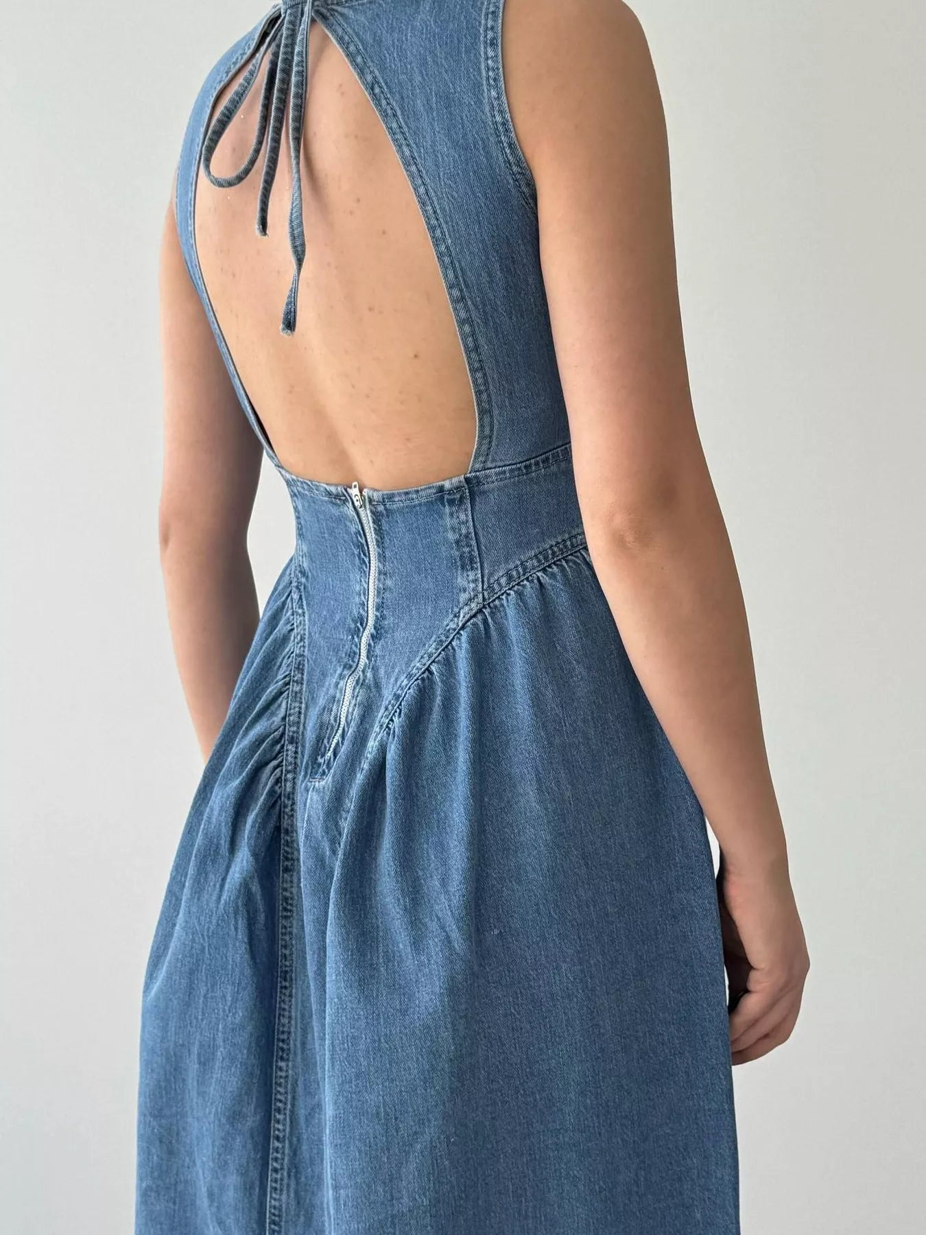 Dark blue sleeveless denim midi dress with open back, tie and back zip, back view
