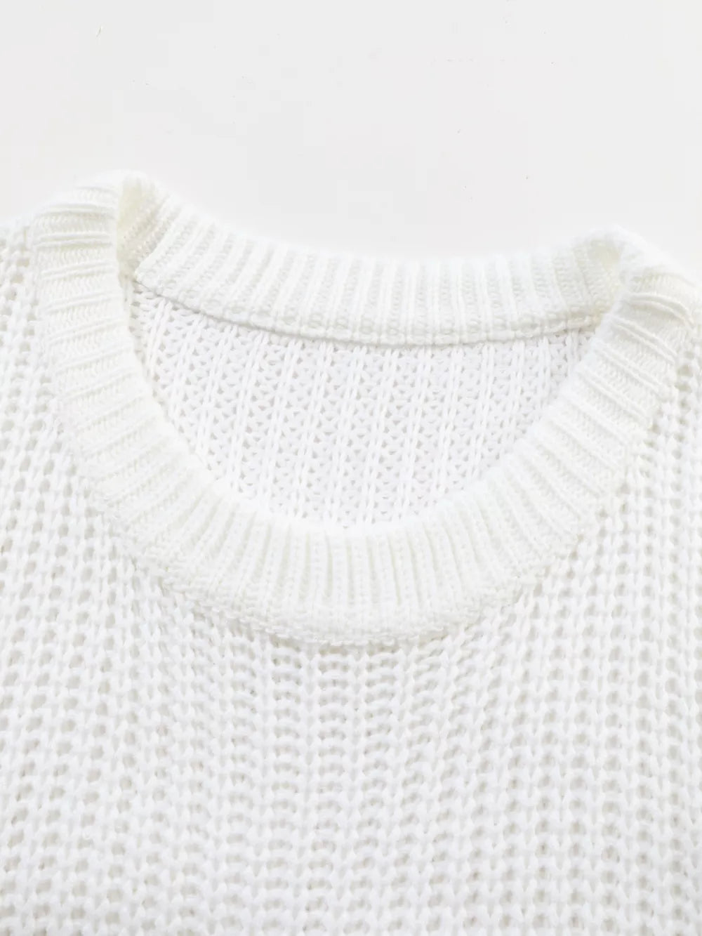 Close view of white ribbed knit sweater showing round neckline and open knit texture.