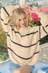Cream oversize striped sweater worn seated outdoors with arms raised above head