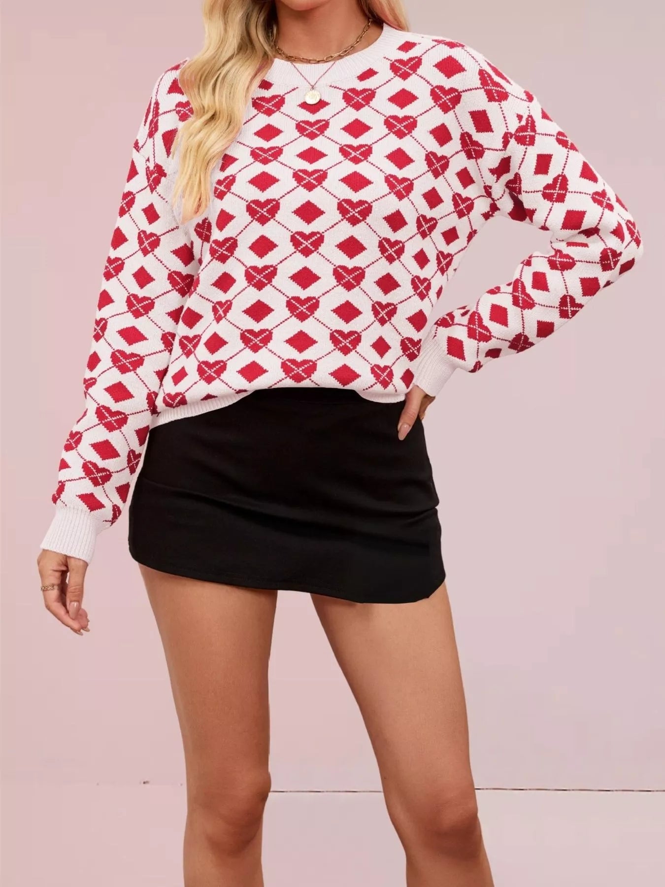 Front view of a white knit sweater with red heart and diamond argyle pattern, hand on hip