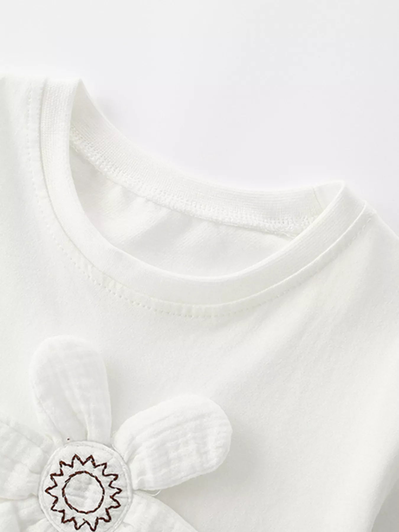 Close-up of white children's t-shirt neckline and upper edge of padded flower applique