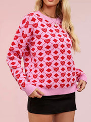 On-model front view of a pink knit sweater with red heart argyle pattern, hands at hem
