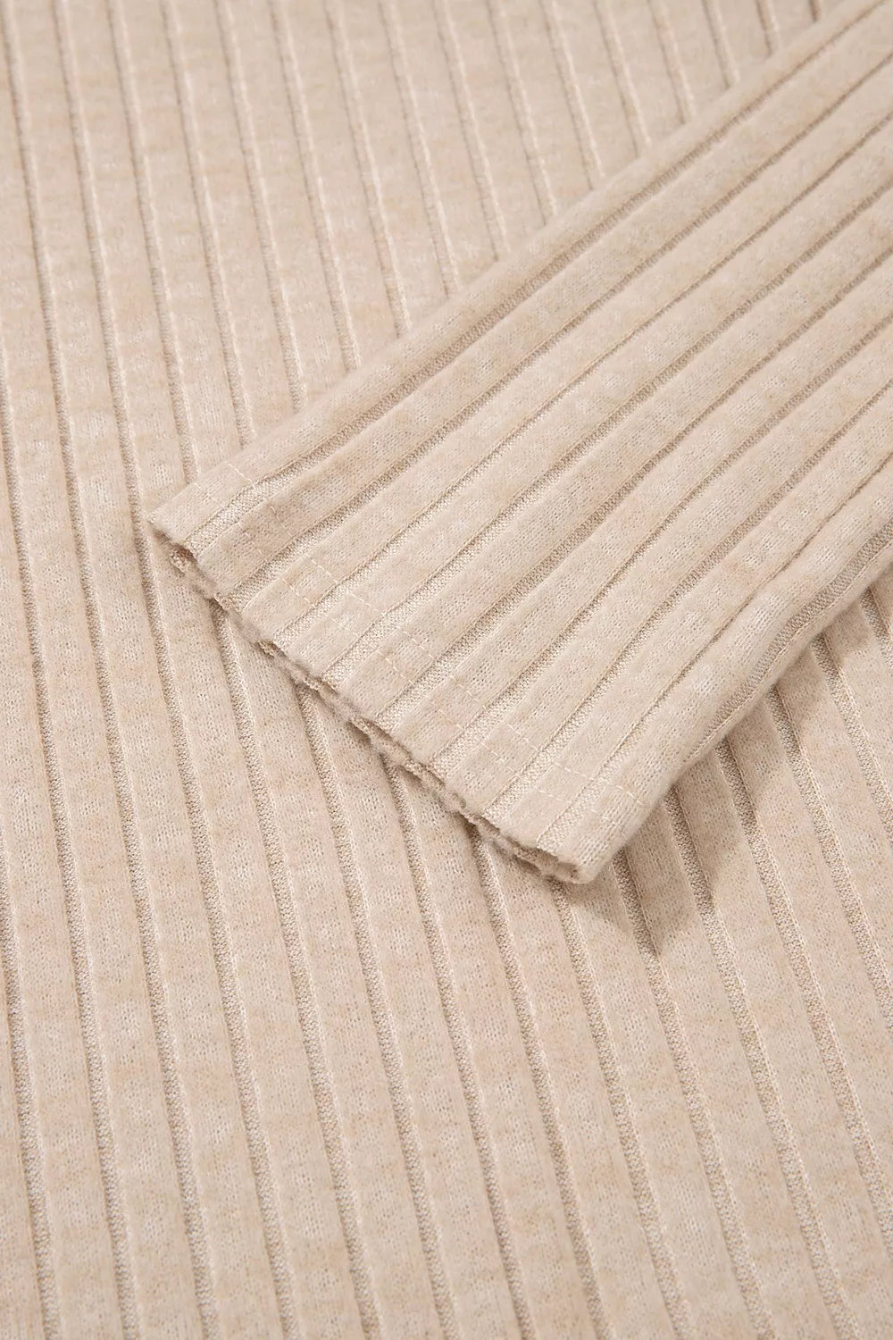 Close-up detail of a beige ribbed knit fabric showing the long sleeve top’s texture and folded edge
