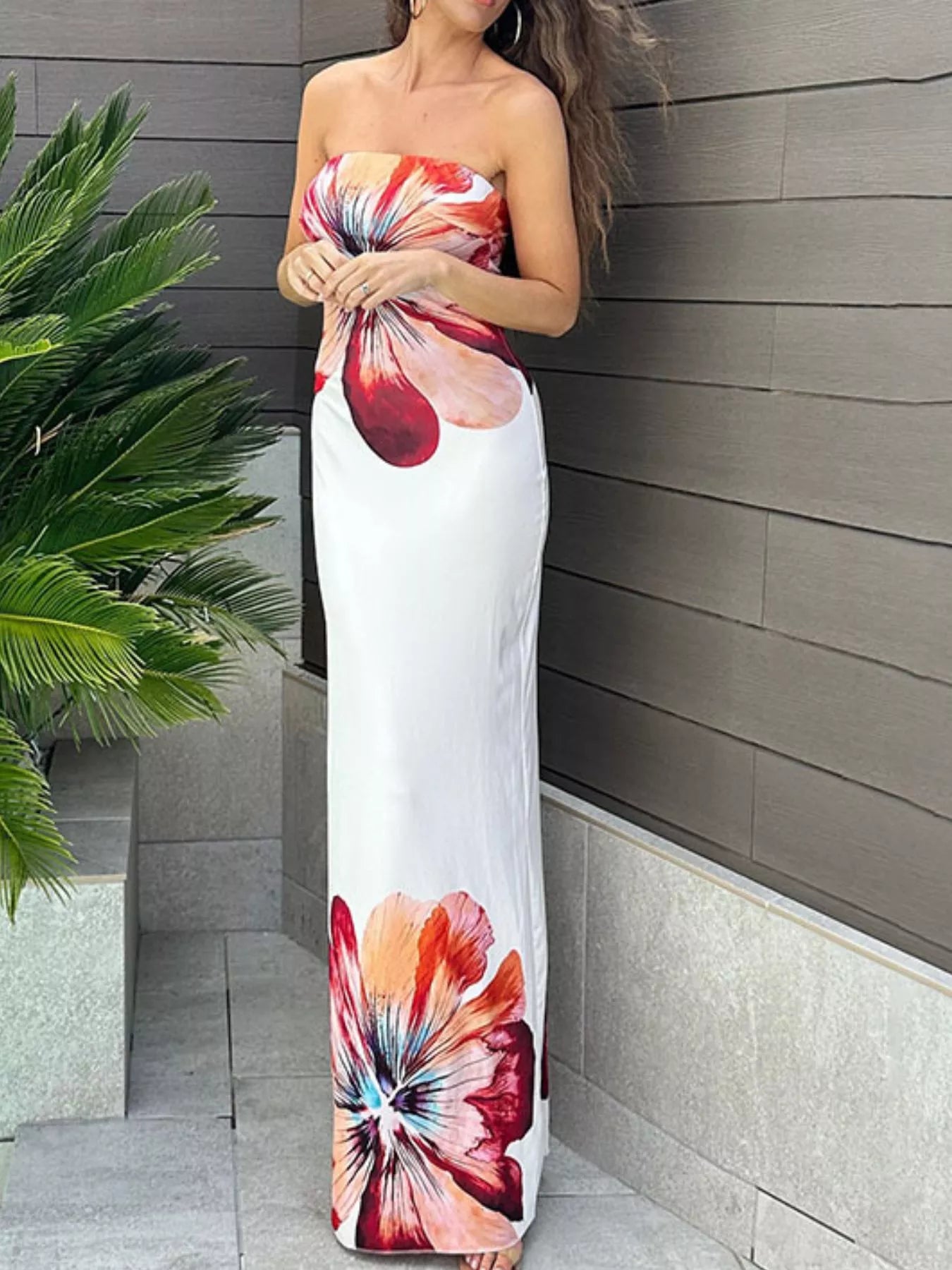 Front view of strapless bodycon maxi dress with large floral print beside a palm plant