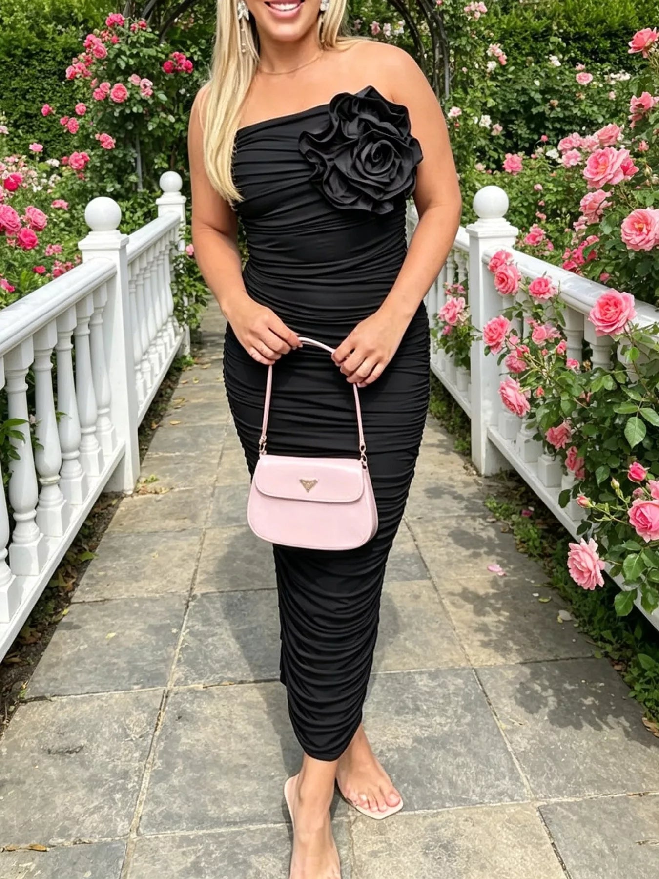Front view of black ruched tube bodycon midi dress with large flower detail outdoors