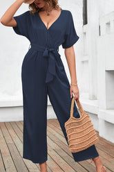 Women's navy short-sleeve jumpsuit with a surplice neckline, tied waist, and wide legs.