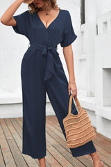 Women's navy short-sleeve jumpsuit with a surplice neckline, tied waist, and wide legs.