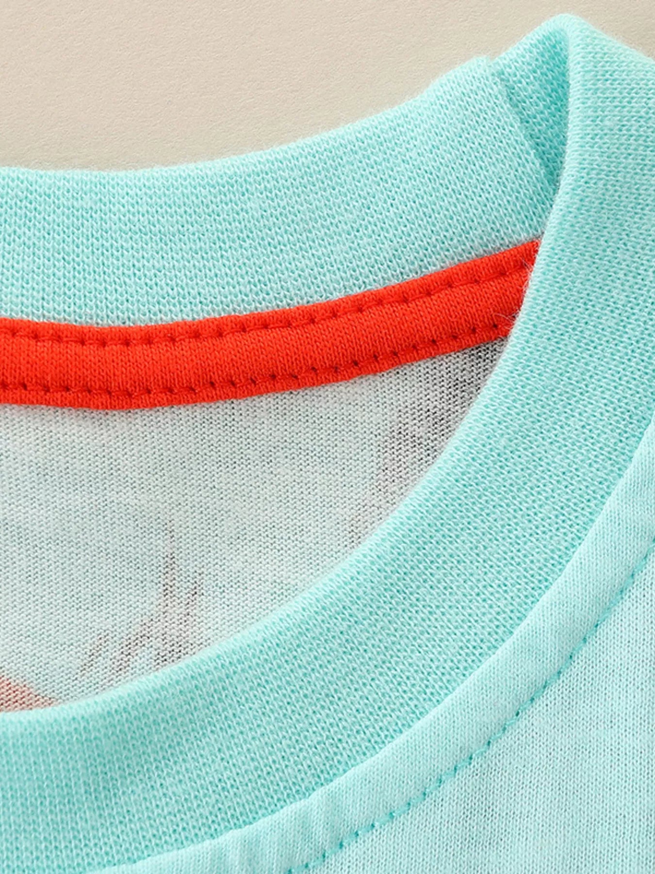 Close-up of the ribbed round neckline with red inner trim and soft aqua knit fabric