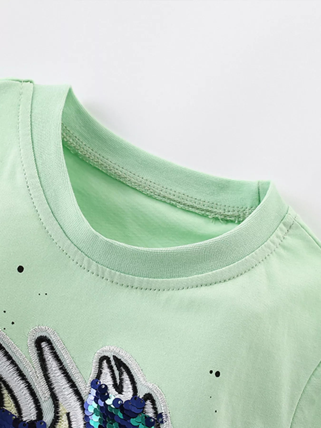Close-up of ribbed crew neckline and stitching on light green children's tee