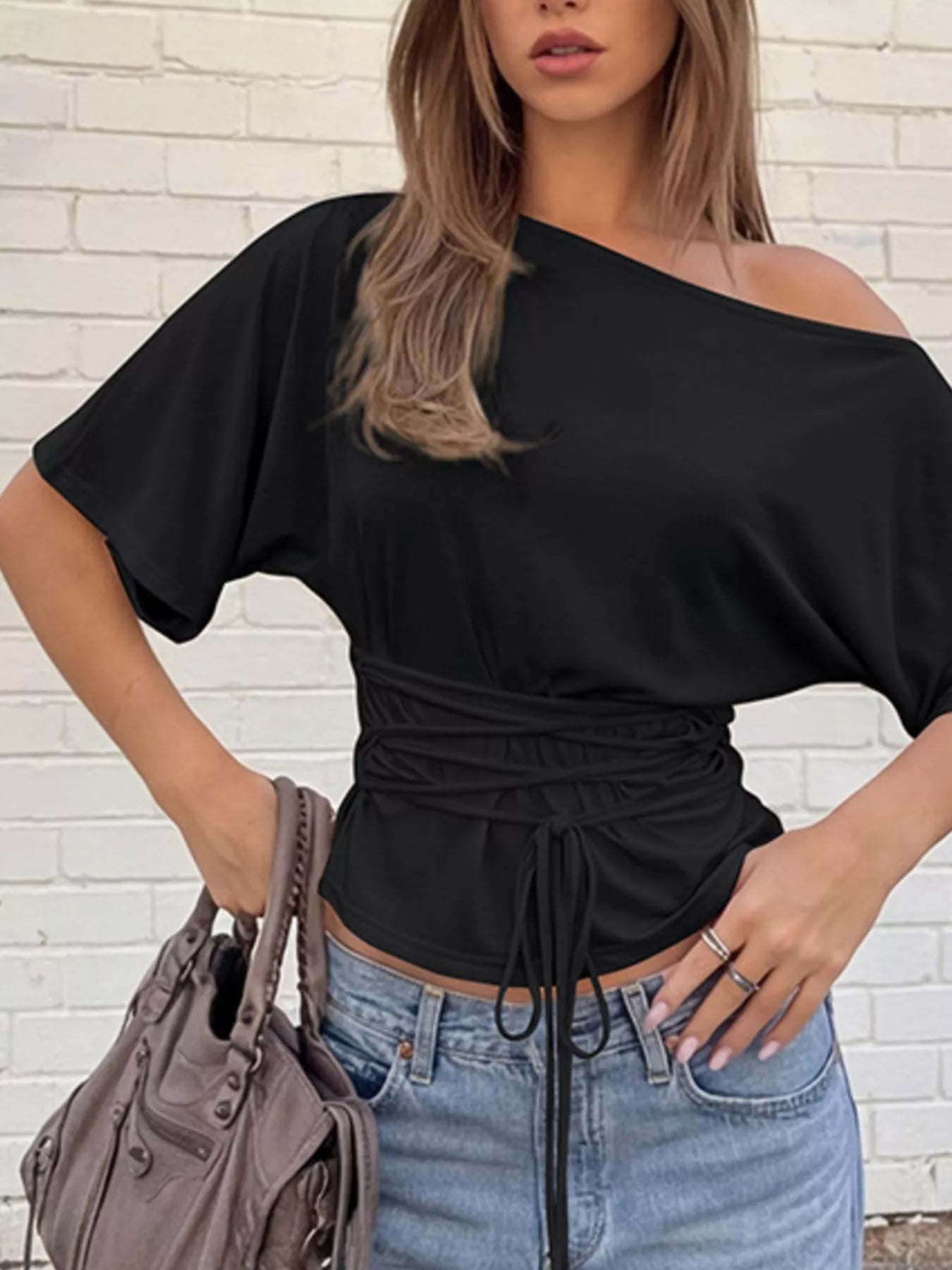Black boat-neck short-sleeve T-shirt styled with jeans, featuring a ruched waist and front tie.
