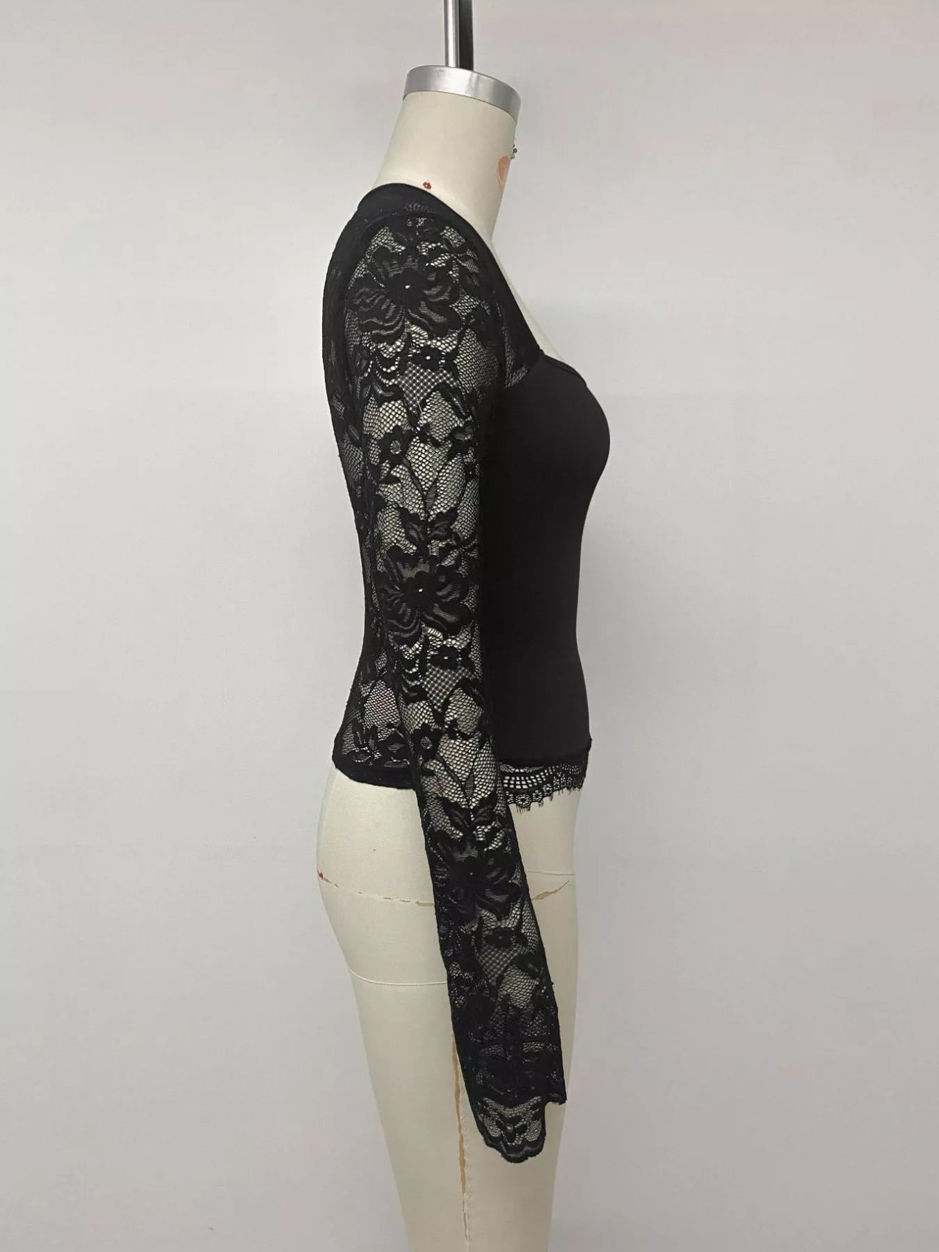 Side view of black square-neck top with sheer floral lace long sleeves and scalloped hem.