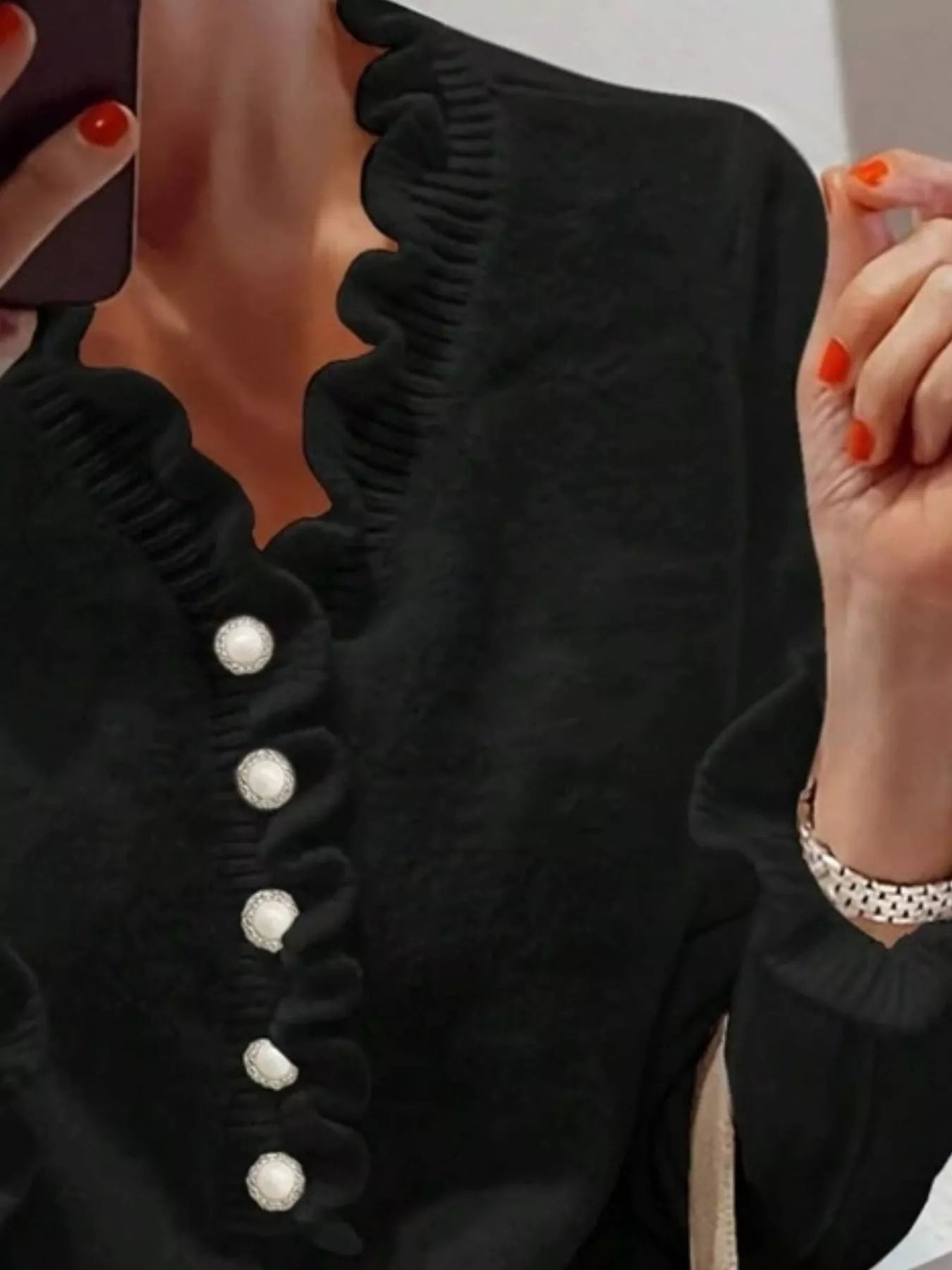 Close front view of a black ruffled sweater with pearl buttons